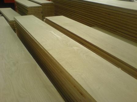 Stosy jasnej tarcicy budowlanej ułożone w magazynie, widoczne słoje drewna i krawędzie desek.